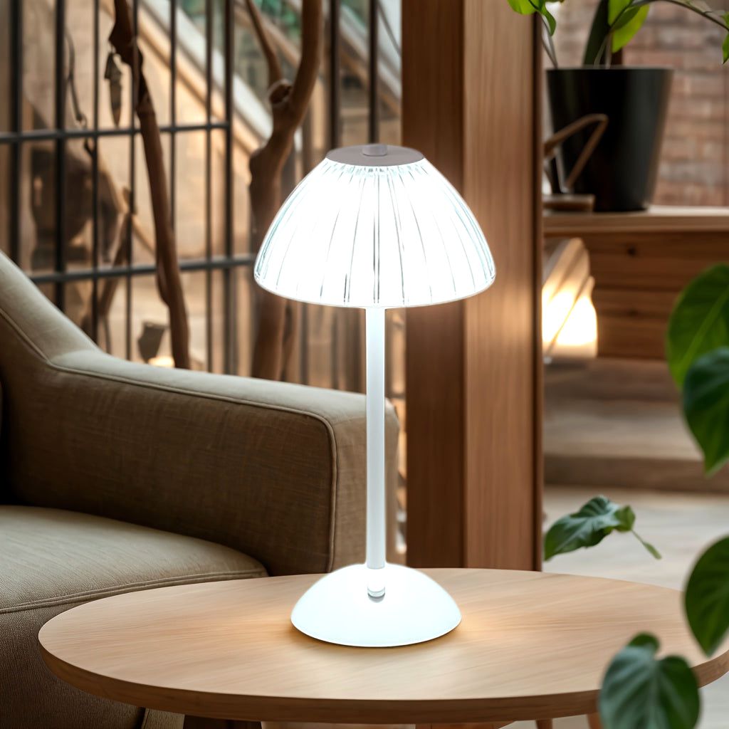 Luxe Glow USB rechargeable table lamp with a white finish and pleated shade, illuminated on a round wooden side table next to a comfortable beige armchair.