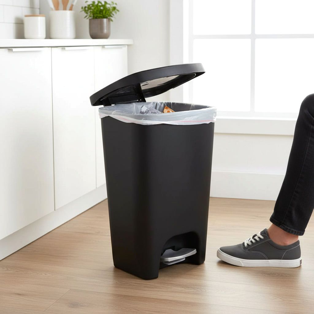 A black Serenity kitchen trash can with its lid open, revealing a trash bag inside, positioned in a modern kitchen setting with a person's foot nearby.