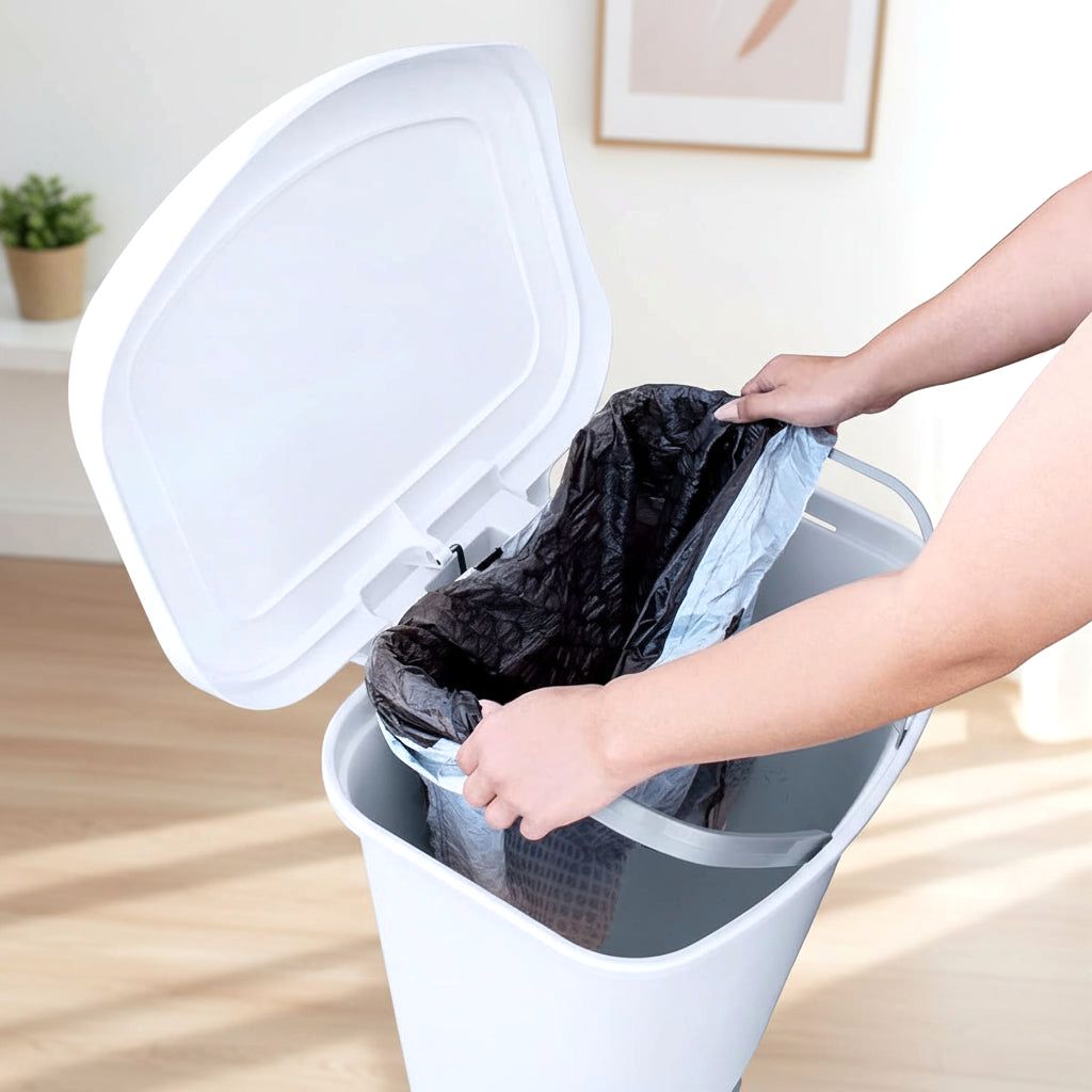 A pair of hands placing a black trash bag into the open lid of a white Serenity kitchen trash can, demonstrating easy bag insertion.